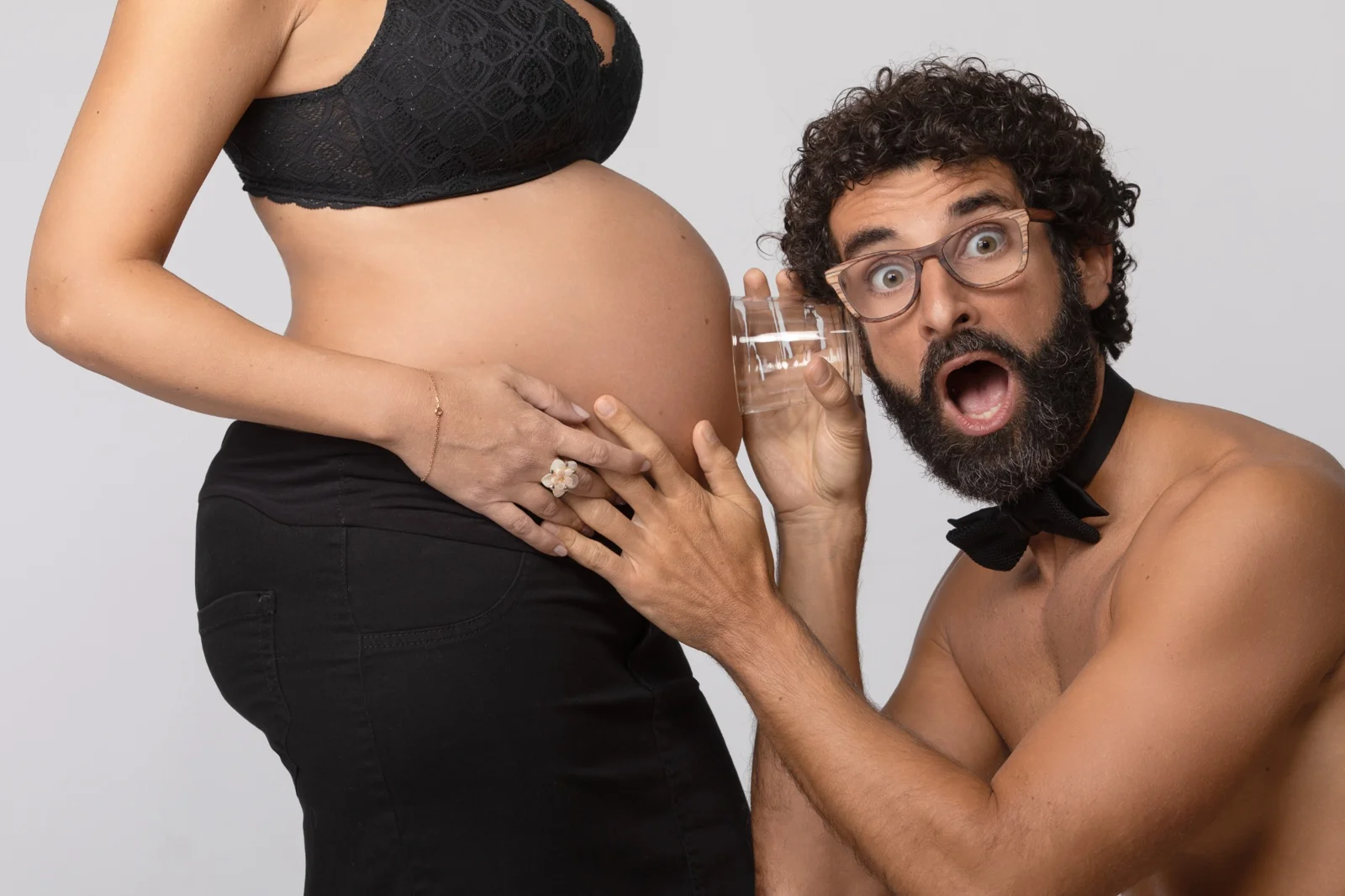 Papa divertito ascolta la pancia della futura mamma durante un servizio fotografico di gravidanza a Milano